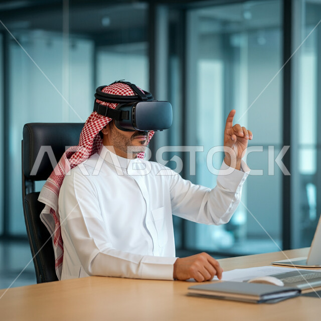 التفاعل والاندماج ومحاكاة العالم الخيالي، رجل عربي خليجي سعودي يرتدي الثوب التقليدي والشماغ يجلس امام مكتبه يرتدي نظارة الواقع الافتراضي يشير باصبع السبابة للاعلى، استخدام حاسة اللمس لملامسة عنصر ما بإيماءات النقر، استخدام التقنية والاجهزة الحديثة