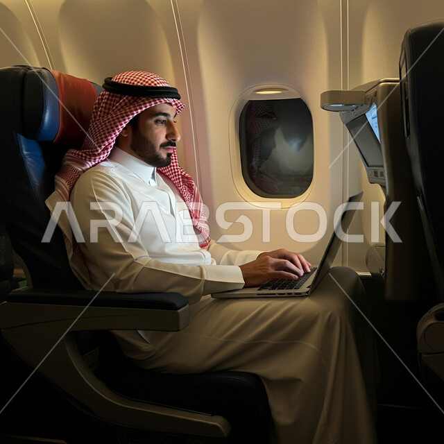 التواصل مع الأهل والاصدقاء عبر اللابتوب، انجاز مهام العمل عن بعد بايماءات الاندماج، صورة من الجانب لرجل عربي خليجي سعودي يرتدي الثوب التقليدي والشماغ يجلس في الطائرة ويعمل على الحاسب المحمول، استخدام الأجهزة والتقنيات الحديثة، مفهوم السياحة والسفر