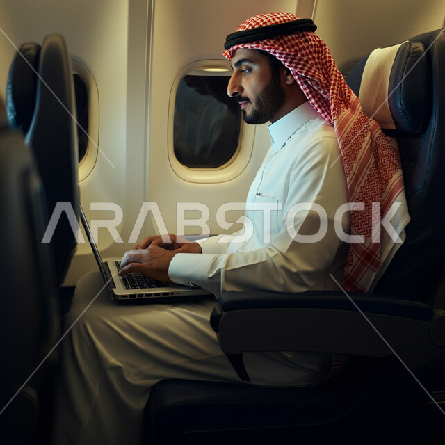 التواصل مع الأهل والاصدقاء عبر اللابتوب، انجاز مهام العمل عن بعد بايماءات الاندماج، صورة من الجانب لرجل عربي خليجي سعودي يرتدي الثوب التقليدي والشماغ يجلس في الطائرة ويعمل على الحاسب المحمول، استخدام الأجهزة والتقنيات الحديثة، مفهوم السياحة والسفر