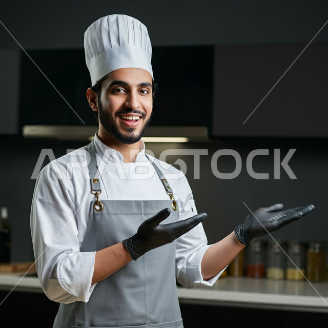 احتراف مهنة وفنون الطبخ، صورة مقربة لشيف عربي خليجي سعودي يرتدي زي الطهاة يعمل في المطبخ ينظر إلى الكاميرا بتعابير السعادة والسرور، الفن في إعداد وتقديم الأصناف المتنوعة، العمل في مطابخ ومطاعم المملكة العربية السعودية