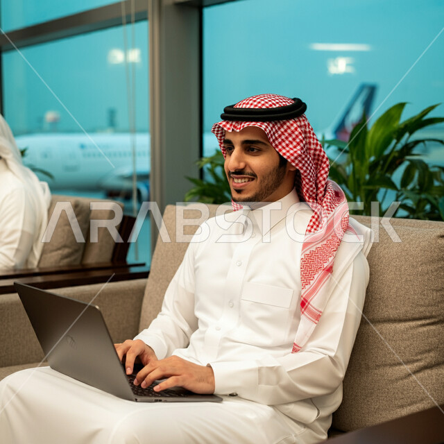 إنجاز العمل من خلال جهاز اللابتوب, قضاء عطلة صيفية ممتعة، مفهوم الرحلات الجوية السياحية, رجل أعمال عربي سعودي خليجي مبتسم يرتدي الثوب التقليدي داخل صالة الانتظار في المطار, الاستعداد للسفر في رحلة عمل, أهمية السياحة في المملكة العربية السعودية