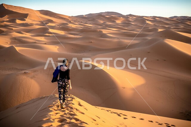 أماكن المغامرات والرحلات السياحية الممتعة, البيئة الصحراوية في المملكة العربية السعودية, التشكيلات والتكوينات الرملية في الصحراء, صورة من الخلف لإمرأة عربية خليجية سعودية تقوم بقضاء وقت ممتع في التجول فوق الكثبان والرمال الذهبية
