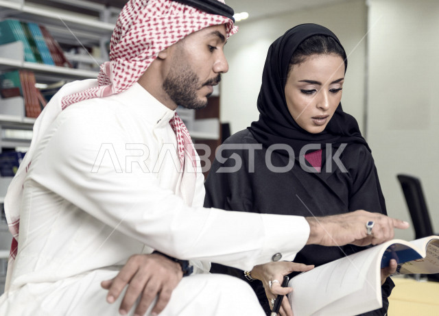 طالبان جامعيان  عربيان سعوديان خليجيان في مكتبة الجامعة، قراءة كتاب داخل المكتبة، الإستعداد للإمتحانات, تدوين الملاحظات, مشاركة المعلومات, استعارة كتاب مناسب، الدراسه الجماعيه في مكتبة الجامعه,  مناقشة المواد الدراسيه، البحث العلمي، مفهوم العلم والتعلم