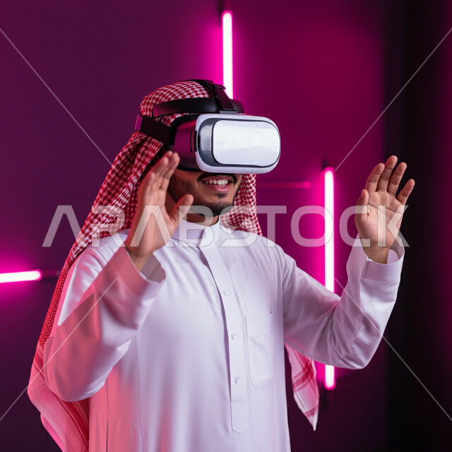 الاندماج والتفاعل ومحاكاة العالم الخيالي، رجل عربي خليجي سعودي مبتسم يرتدي الثوب التقليدي والشماغ يضع نظارات الفي ار يرفع يديه للاعلى بايماءات الدفاع عن النفس، محاولة امساك ولمس شيء ما، استخدام التقنية والاجهزة الحديثة