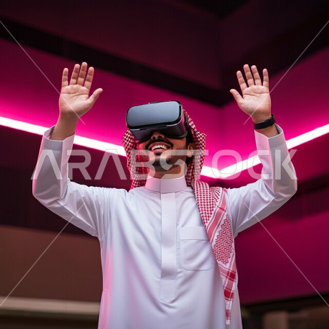 Integration, interaction and simulation of the imaginary world, a smiling Saudi Arabian Gulf man wearing the traditional thobe and shemagh, wearing VR glasses, raising his hands up with self-defense gestures, trying to grab and touch something, using modern technology and devices
