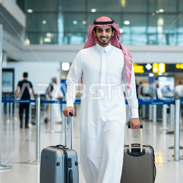 الاستعداد للذهاب في رحلة ترفيهية، رجل عربي خليجي سعودي يرتدي الشماغ والثوب التقليدي يمسك بيده حقيبة الامتعة ينظر إلى الكاميرا بإيماءات السعادة والسرور، صالة الانتظار في مطارات المملكة العربية السعودية، قضاء إجازة صيفية ممتعة، الاناقة والاهتمام بالمظهر الخارجي