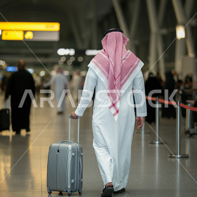 مفهوم السياحة والسفر، الاستعداد للذهاب في رحلة ترفيهية، صورة من الخلف لرجل عربي خليجي سعودي يرتدي الشماغ والثوب التقليدي يمسك بيده حقيبة الامتعة، صالة الانتظار في مطارات المملكة العربية السعودية، قضاء إجازة صيفية ممتعة، الجسم الكامل بالطول