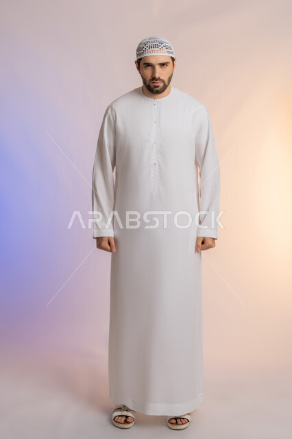 النظر الى الكاميرا بايماءات الغضب والانزعاج، الاهتمام بالمظهر الخارجي, مفهوم الأناقة والرجولة, بورتريه لرجل عربي خليجي اماراتي يرتدي الكندورة  والقبعة يقف باستقامة واعتدال، التقاط الصور الشخصية للوثائق الرسمية، خلفية ملونة