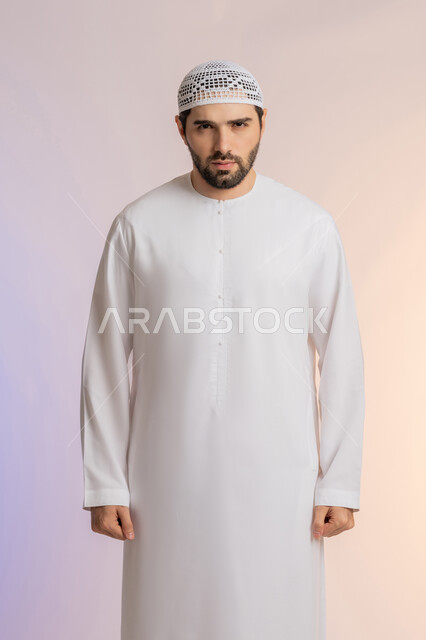 النظر الى الكاميرا بايماءات الغضب والانزعاج، الاهتمام بالمظهر الخارجي, مفهوم الأناقة والرجولة, بورتريه لرجل عربي خليجي اماراتي يرتدي الكندورة  والقبعة يقف باستقامة واعتدال، التقاط الصور الشخصية للوثائق الرسمية، خلفية ملونة