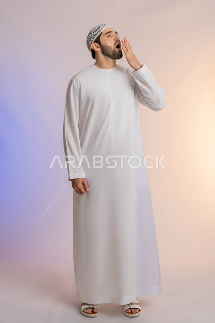الشعور بالنعاس والحاجة للنوم، ضرورة أخذ قسط من الراحة والاسترخاء، إيماءات التعب والإرهاق، بورتريه لرجل عربي خليجي اماراتي يرتدي الكندورة والطاقية البيضاء يقوم بوضع يضع يده أمام فمه والتثاؤب، خلفية ملونة