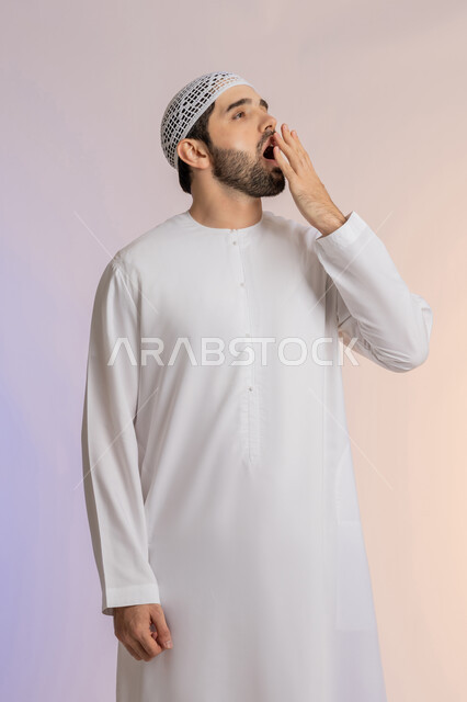 الشعور بالنعاس والحاجة للنوم، ضرورة أخذ قسط من الراحة والاسترخاء، إيماءات التعب والإرهاق، بورتريه لرجل عربي خليجي اماراتي يرتدي الكندورة والطاقية البيضاء يقوم بوضع يضع يده أمام فمه والتثاؤب، خلفية ملونة