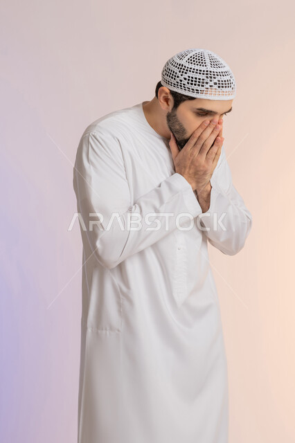 المفاجأة و الصدمة عند رؤية شيء ما، الانزعاج عند سماع خبر سيء, الوقوع في مصيبة, النظر الى الكاميرا بتعابير التعجب, بورتريه لرجل عربي خليجي اماراتي يرتدي الكندورة والقبعة يضع يديه على فمه رأس بتعابير الدهشة و الذهول، خلفية ملونة