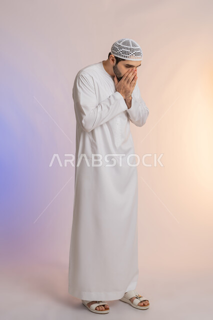 المفاجأة و الصدمة عند رؤية شيء ما، الانزعاج عند سماع خبر سيء, الوقوع في مصيبة, النظر الى الكاميرا بتعابير التعجب, بورتريه لرجل عربي خليجي اماراتي يرتدي الكندورة والقبعة يضع يديه على فمه رأس بتعابير الدهشة و الذهول، خلفية ملونة