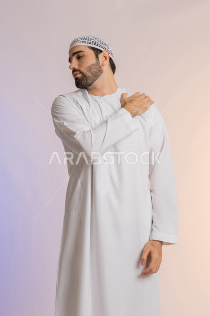 التهاب العضلات والمفاصل، الإحساس بالتعب والإرهاق, إيماءات الألم في الأكتاف، بورتريه من الخلف لرجل عربي خليجي اماراتي يرتدي الكندورة والقبعة البيضاء  يضع يده على كتفه بتعابير الوجع، الحاجه لوضع خطة علاجية, طلب المساعده للذهاب الى المستشفى، خلفية ملونة