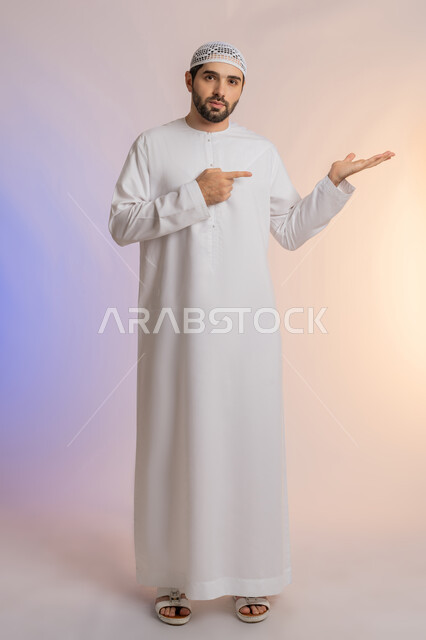 رفع وحمل عنصر معين، تحديد شيء معين بإيماءات السرور والسعادة، بورتريه لرجل عربي خليجي اماراتي يرتدي الكندورة والقبعة البيضاء يفتح كفه للأعلى ويشير إلى عنصر ما, حمل عنصر هولوجرامي، خلفيه ملونة