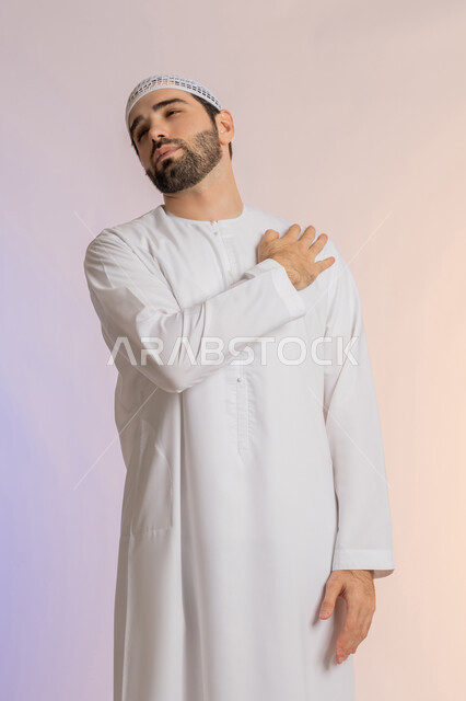 التهاب العضلات والمفاصل، الإحساس بالتعب والإرهاق, إيماءات الألم في الأكتاف، بورتريه من الخلف لرجل عربي خليجي اماراتي يرتدي الكندورة والقبعة البيضاء  يضع يده على كتفه بتعابير الوجع، الحاجه لوضع خطة علاجية, طلب المساعده للذهاب الى المستشفى، خلفية ملونة