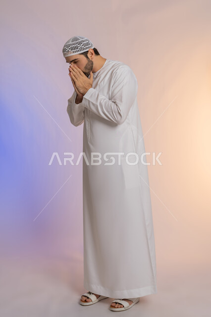 التهاب الأنف التحسسي, الشعور بالمرض و الزكام والحاجة الى العلاج والدواء, بورتريه لشاب عربي خليجي اماراتي يرتدي الكندورة  والقبعة يضع يديه على وجهه بإيماءات العطاس, صوة الجسم بالطول الكامل، خلفية ملونة