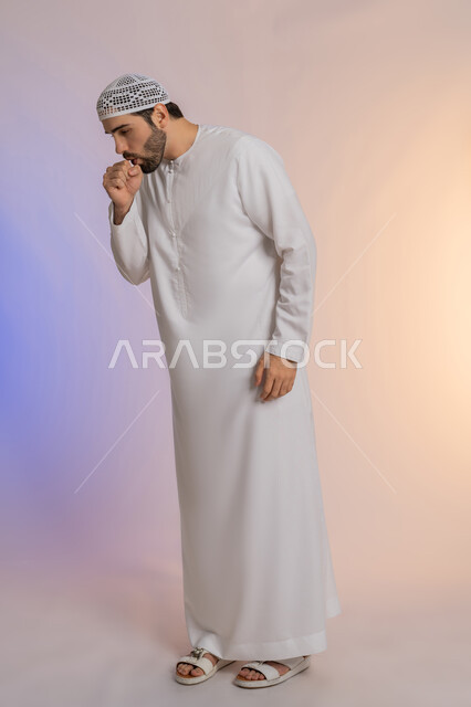 التهاب الصدر التحسسي, الشعور بالمرض و الزكام والحاجة الى العلاج والدواء, بورتريه لشاب عربي خليجي اماراتي يرتدي الكندورة والقبعة يضع يديه على وجهه بإيماءات السعال, صوة الجسم بالطول الكامل، خلفية ملونة