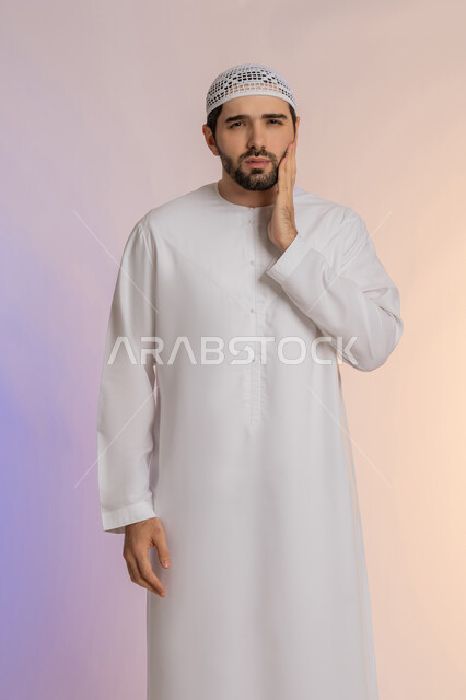 الاشارة إلى الفم بتعابير الإرهاق والتعب, مشاكل التهاب اللثة وتسوس الأسنان, بورتريه لرجل عربي خليجي اماراتي يرتدي الكندورة والقبعة ينظر الى الكاميرة بإيماءات الانزعاج والألم الشديد،  خلفية ملونة