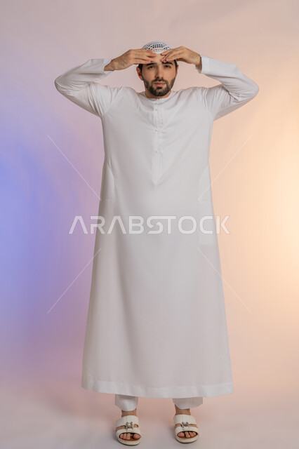 التعرض للتعب والإرهاق والعمل الطويل، آلام الصداع النصفي، التعرض لنوبات الشقيقة الحادة, الحاجة لتناول المسكنات وأخذ قسط من الراحة، بورتريه لرجل عربي خليجي اماراتي يرتدي الكندورة والقبعة يمسك رأسه بيديه بإيماءات الألم، الجسم بالطول الكامل خلفية ملونة
