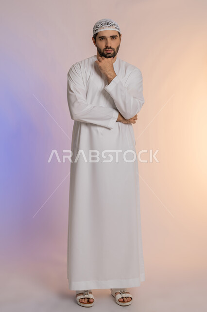 Solving problems and making decisions, looking forward and planning for the future, portrait of an Arab Gulf Emirati man wearing a kandura and a hat, placing his hand on his chin with gestures of thought and absent-mindedness, the concept of listening and focusing, full-length body, colored background