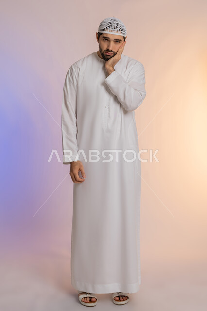 مشاكل التهاب اللثة وتسوس الأسنان, الاشارة إلى الفم بتعابير الإرهاق والتعب, بورتريه لرجل عربي خليجي اماراتي يرتدي الكندورة والقبعة ينظر الى الكاميرة بإيماءات الانزعاج والألم الشديد، صورة الجسم بالطول الكامل، خلفية ملونة