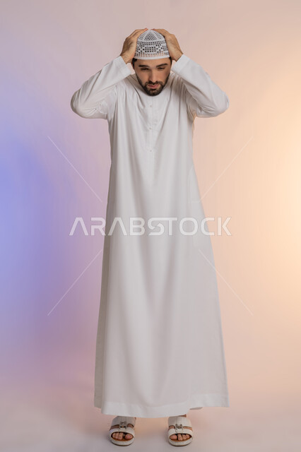 آلام الصداع النصفي، التعرض لنوبات الشقيقة الحادة، الحاجة لتناول المسكنات وأخذ قسط من الراحة، التعرض للتعب والإرهاق والعمل الطويل، بورتريه لرجل عربي خليجي اماراتي يرتدي الكندورة والقبعة يمسك رأسه بيديه بإيماءات الألم، الجسم بالطول الكامل، خلفية ملونة