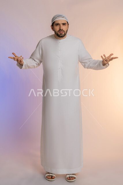 فتح اليدين في دلالة على الاستسلام، القلق والحيرة في اتخاذ القرار الصحيح، محاولة إيجاد حل للمشكلات العصبة، بورتريه لرجل عربي خليجي اماراتي  يرتدي الكندورة والقبعة ينظر إلى الكاميرا ويقف باستقامة، الجسم بالطول الكامل، خلفية ملونة