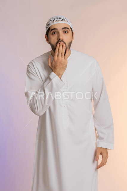 التعرض لصدمة وعدم التصديق، إيماءات الدهشة والمفاجأة، الاهتمام بالمظهر الخارجي، خيبة الأمل والمشاعر السلبية، بورتريه لرجل عربي خليجي اماراتي يرتدي الكندورة والقبعة يضع يده أمام فمه، خلفية ملونة