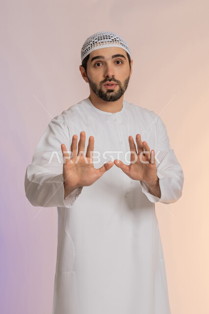 طلب التوقف عن فعل شيء ما، الأمر بالوقوف وعدم التمادي، الرفض وعدم الخضوع، النهي عن التقدم وأهمية ترك مسافة أمان، بورتريه لرجل عربي خليجي اماراتي يرتدي الكندورة والقبعة البيضاء يرفع كفه للأعلى بإيماءات الغضب والجدية،  خلفية ملونة