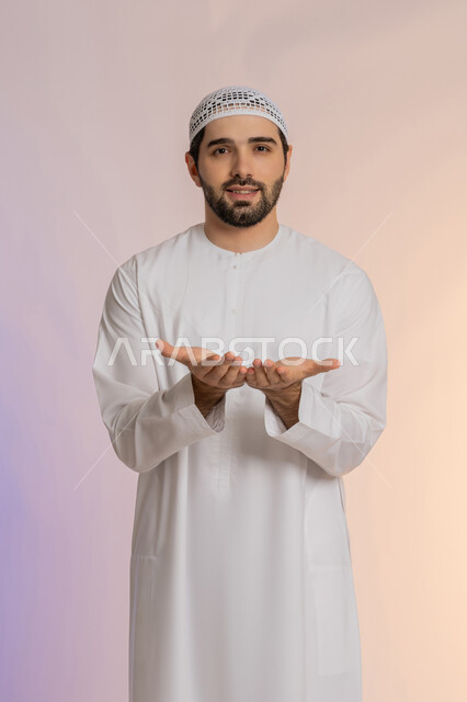 فتح الكفين ومدهما محو الأمام، تقديم الضيافة أو إعطاء شيء ما، الأناقة والوسامة والرجولة، مفهوم التقدير والاحترام، بورتريه لرجل عربي خليجي اماراتي يرتدي الكندورة والقبعة البيضاء ينظر إلى الكاميرا بإيماءات السعادة والسرور،  خلفية ملونة