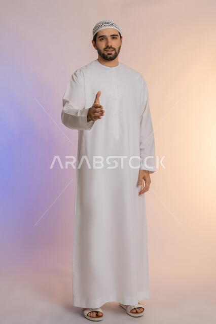 مد كف اليد نحو الأمام للمصافحة، إلقاء التحية والسلام، الأناقة والوسامة والرجولة، مفهوم التقدير والاحترام، بورتريه لرجل عربي خليجي اماراتي يرتدي الكندورة والقبعة البيضاء ينظر إلى الكاميرا بإيماءات السعادة والسرور، خلفية ملونة