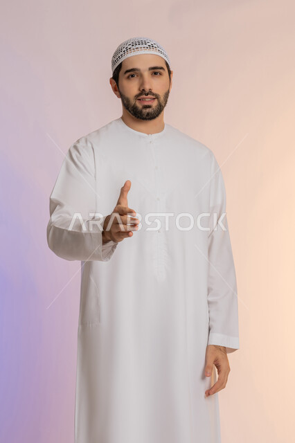 مد كف اليد نحو الأمام للمصافحة، إلقاء التحية والسلام، الأناقة والوسامة والرجولة، مفهوم التقدير والاحترام، بورتريه لرجل عربي خليجي اماراتي يرتدي الكندورة والقبعة البيضاء ينظر إلى الكاميرا بإيماءات السعادة والسرور، خلفية ملونة