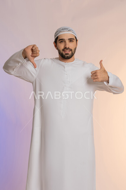 علامة الجودة والسوء، الإشارة باصبعي الابهام إلى جهتين متعاكستين، الحيرة في اتخاذ القرار الصحيح، الرضا وعدم الاستحسان، بورتريه لرجل عربي خليجي اماراتي يرتدي الكندورة والقبعة البيضاء وينظر إلى الكاميرا بجدية، خلفية ملونة