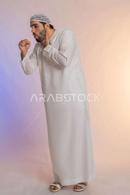 الكحة والتهاب الحلق والحاجة للعلاج، إيماءات الإرهاق والتعب الشديد، الإصابة بالأنفلونزا ونزلات البرد، بورتريه لرجل عربي خليجي اماراتي يرتدي الكندورة والقبعة البيضاء يضع يده أمام فمه ويقوم بالسعال, صورة الجسم بالطول الكامل، خلفية ملونة
