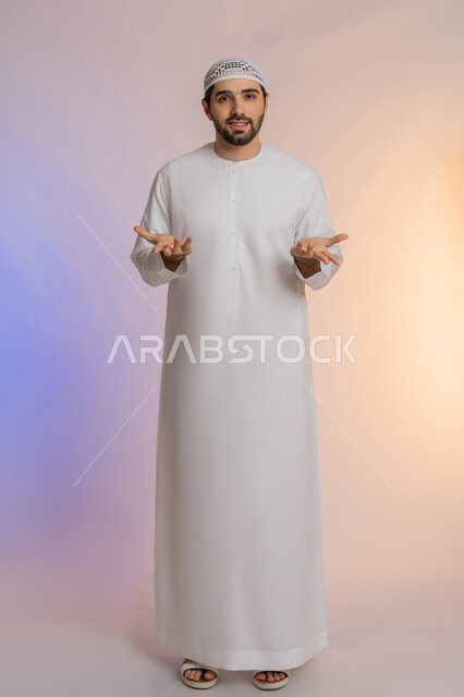 الوقوف بإيماءات التعجب والدهشة، الشعور بالسعادة والسرور لسماع الأخبار المنتظرة، بورتريه لرجل عربي خليجي اماراتي يرتدي الكندورة والقبعة يفتح يديه بتعابير الصدمة والذهول والانبهار، التفاجؤ والاستغراب من شيء ما، الطول الكامل للجسم، خلفية ملونة