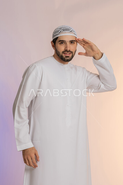 الأناقة والوسامة والرجولة، إلقاء التحية والسلام، مفهوم التقدير والاحترام، بورتريه لرجل عربي خليجي اماراتي مبتسم يرتدي الكندورة والقبعة ينظر إلى الكاميرا بإيماءات السعادة والسرور، الوقوف باستقامة بتعابير الثقة بالنفس، خلفية ملونة
