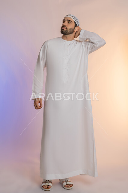 Looking forward and planning, problem solving and decision making, portrait of an Arab Gulf Emirati man wearing a kandura and hat, putting his hand on his neck with gestures of thinking and absent-mindedness, concept of listening and concentration, full-length body image, colored background