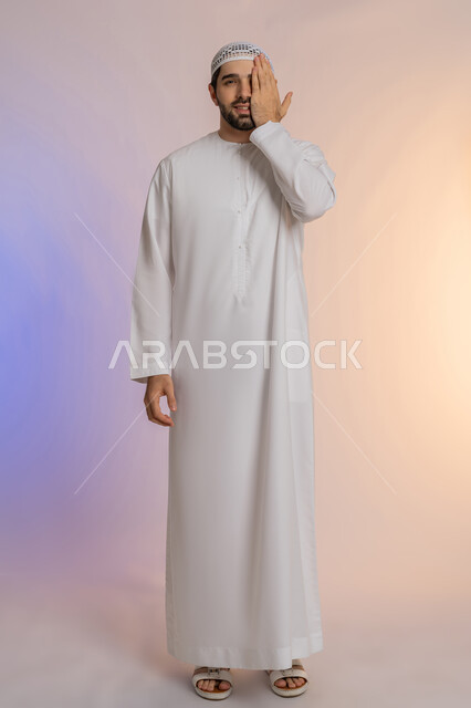 وضع اليد على العين وتغطيها، التهاب واحمرار العيون والحاجة لزيارة الطبيب، ضعف النظر وتشوش الرؤية، التعرض لأذية في الشبكية، بورتريه لرجل عربي خليجي اماراتي يرتدي الكندورة والقبعة يعاني من مشاكل صحية في عينه، الجسم بالطول الكامل، خلفية ملونة