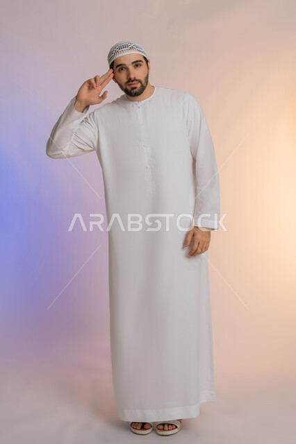 إلقاء التحية والسلام، الأناقة والوسامة والرجولة، مفهوم التقدير والاحترام، بورتريه لرجل عربي خليجي اماراتي مبتسم يرتدي الكندورة والقبعة  ينظر إلى الكاميرا بإيماءات السعادة والسرور، الوقوف باستقامة بتعابير الثقة بالنفس، الجسم بالطول الكامل، خلفية ملونة