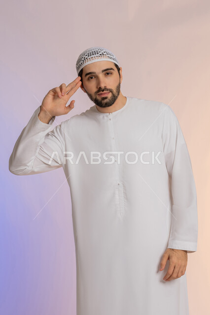 الأناقة والوسامة والرجولة، إلقاء التحية والسلام، مفهوم التقدير والاحترام، بورتريه لرجل عربي خليجي اماراتي مبتسم يرتدي الكندورة والقبعة  ينظر إلى الكاميرا بإيماءات السعادة والسرور، الوقوف باستقامة بتعابير الثقة بالنفس، خلفية ملونة