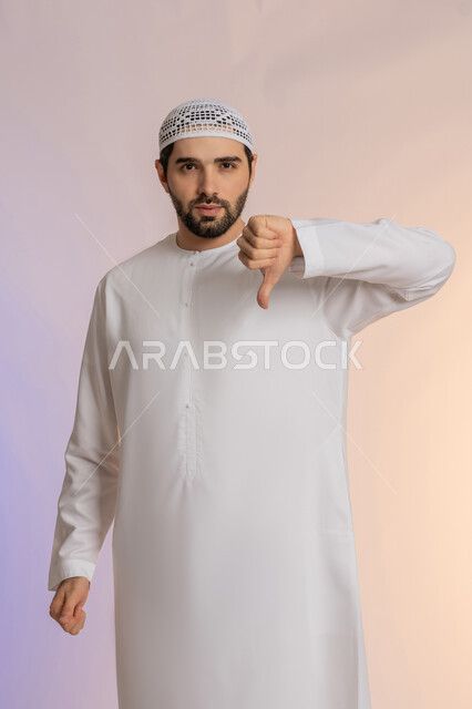 الشعور بالانزعاج والاضطراب, الإشارة باصبع الإبهام نحو الأسفل بعلامات السوء وعدم القبول، التعبير عن الجودة السيئة، بورتريه لرجل عربي خليجي اماراتي يرتدي الكندورة والقبعة  ينظر للكاميرا بإيماءات الغضب، خلفية ملونة