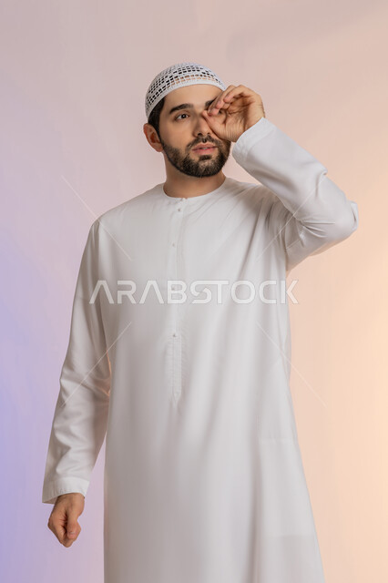 التركيز على شيء ما، محاولة تقريب الأشياء البعيدة، التخطيط للأهداف والطموحات المستقبلية، بورتريه لرجل عربي خليجي اماراتي يرتدي الكندورة والقبعة يضع يده على عينه بشكل عدسة بإيماءات البحث، خلفية ملونة