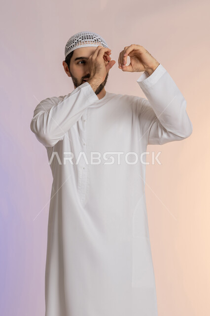 التركيز على شيء ما، محاولة تقريب الأشياء البعيدة، التخطيط للأهداف والطموحات المستقبلية، بورتريه لرجل عربي خليجي اماراتي يرتدي الكندورة والقبعة يضع يده على عينه بشكل عدسة بإيماءات البحث، خلفية ملونة