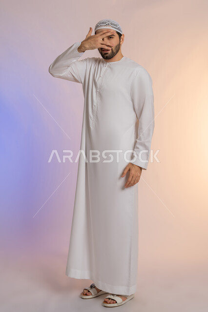 الشعور بالخجل والإحراج، محاولة استراق النظر، البكاء ومشاعر الحزن، إغماض العينين وعدم الرغبة بالرؤية، التعرض لصدمة وعدم التصديق، بورتريه لرجل عربي خليجي اماراتي يرتدي الكندورة والقبعة يغطي وجهه بيده، الجسم بالطول الكامل، خلفية ملونة