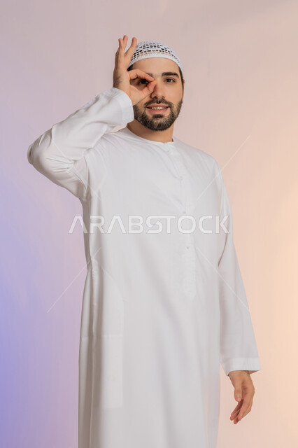 Planning for future goals and ambitions, trying to bring distant things closer, love of discovery, knowledge and adventure, focusing on something, portrait of an Arab Gulf Emirati man wearing a hat, placing his hand over his eye in the shape of a lens with searching gestures, a colored background.