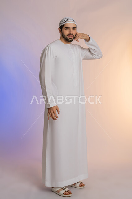 A hand movement indicating communication, the concept of exchanging information, a portrait of an Arab Gulf Emirati man wearing a kandora and wearing a hat, raising his hand with gestures to answer phone calls, receiving good news via mobile phone, full-length body portrait, colored background