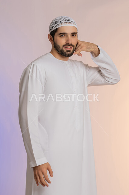 تلقي أخبار سارة عبر الجوال، حركة يد تدل على الاتصال، مفهوم تبادل المعلومات، بورتريه لرجل عربي خليجي اماراتي يرتدي الكندورة ويضع القبعة يرفع يده بايماءات الرد على المكالمات الهاتفية، خلفية ملونة