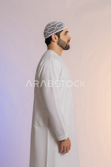 مفهوم الأناقة والرجولة, الاهتمام بالمظهر الخارجي, النظر الى مكان ما بايماءات الثقة بالنفس، بورتريه من الجانب لرجل عربي خليجي اماراتي يرتدي الكندورة والقبعة يقف باستقامة واعتدال, خلفية ملونة