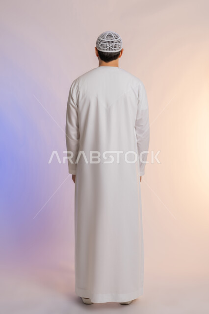 مفهوم الأناقة والرجولة, الاهتمام بالمظهر الخارجي,  بورتريه من الخلف لرجل عربي خليجي اماراتي يرتدي الكندورة ويضع القبعة يقف باستقامة واعتدال, الجسم بالطول الكامل, خلفية ملونة